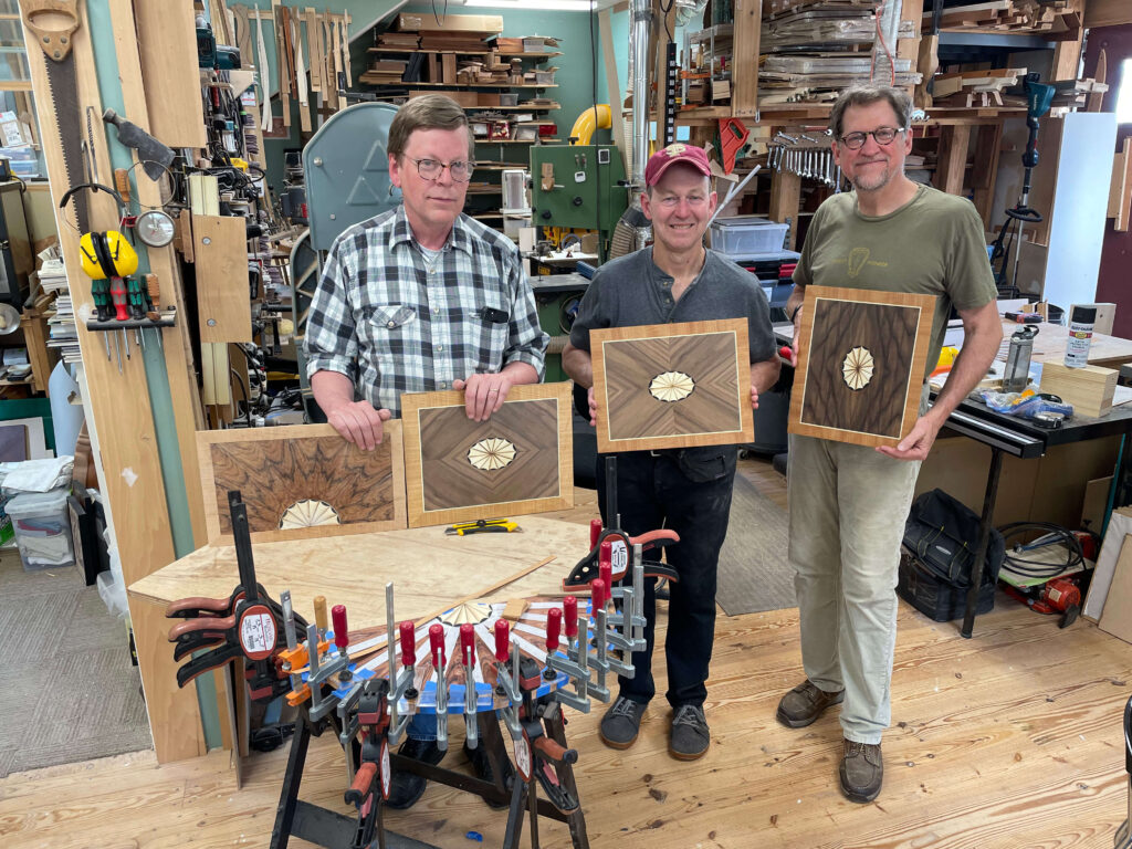 Three woodworkers show the final products from their marquetry class Veneering for Furniture Makers